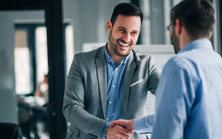 Two smiling men shaking hands at a company reception desk