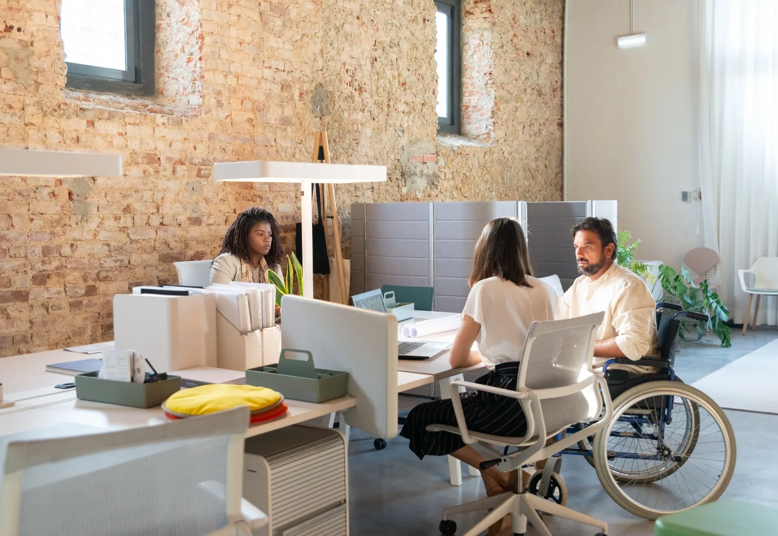 Employees working in a shared office space, including a wheelchair user, illustrating an accessible working environment.