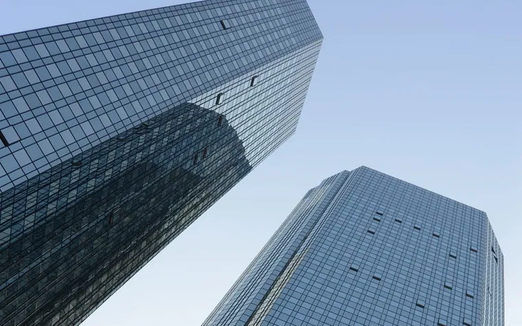 Two glass office towers seen from below against a blue sky