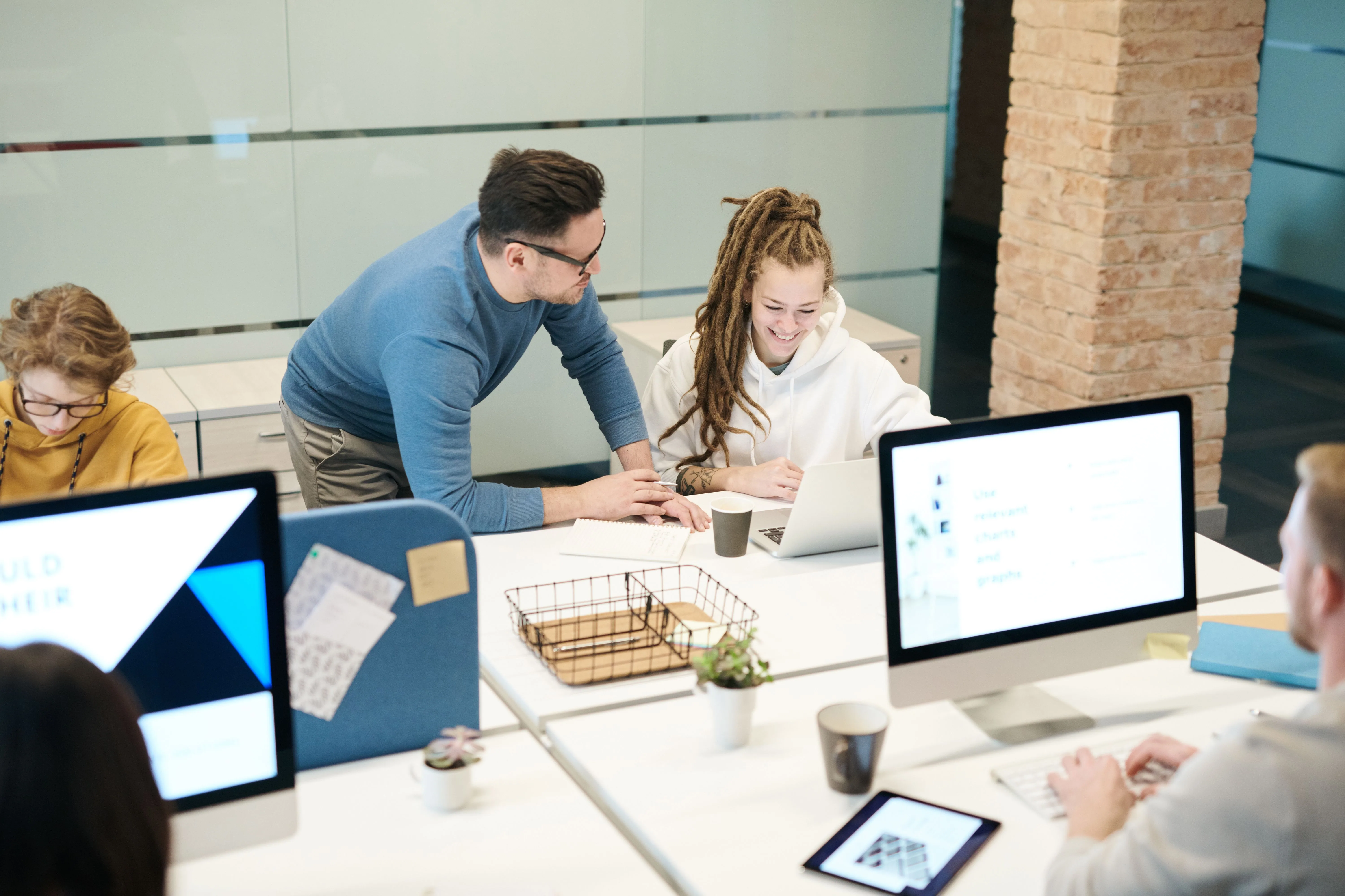 Team of colleagues talking around computers in a modern open-plan office, illustrating collaboration and new ways of working.